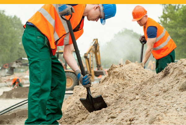 Workers in safety gear digging with shovels at construction site