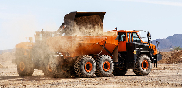 A DEVELON wheel loader dumps material into a DEVELON articulated dump truck (ADT) on a job site.