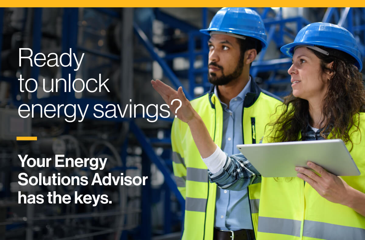 Ready to unlock energy savings? Your Energy Solutions Advisor has the keys: Two workers in hard hats, one holding a tablet device, observing a large mechanical room.